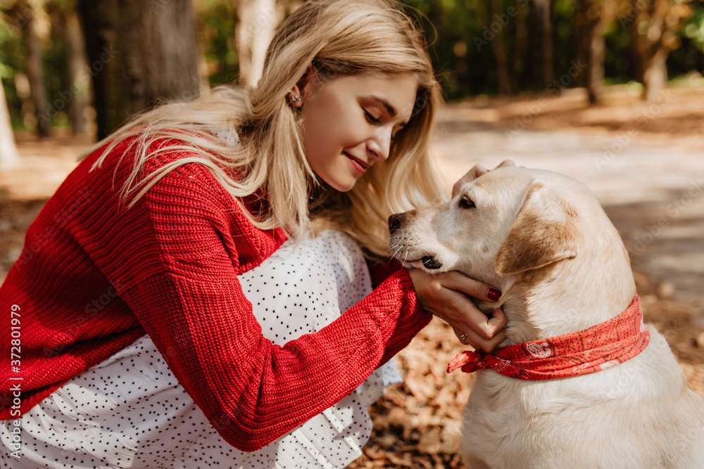 Young blonde woman smiling at her dog. Pretty girl sharing good moments with a pet in the park. Young blonde woman smiling at her dog. Pretty girl sharing good moments with a pet in the park.