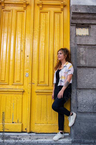 Cheerful latin young woman leaning on a rich colorful yellow door in the street