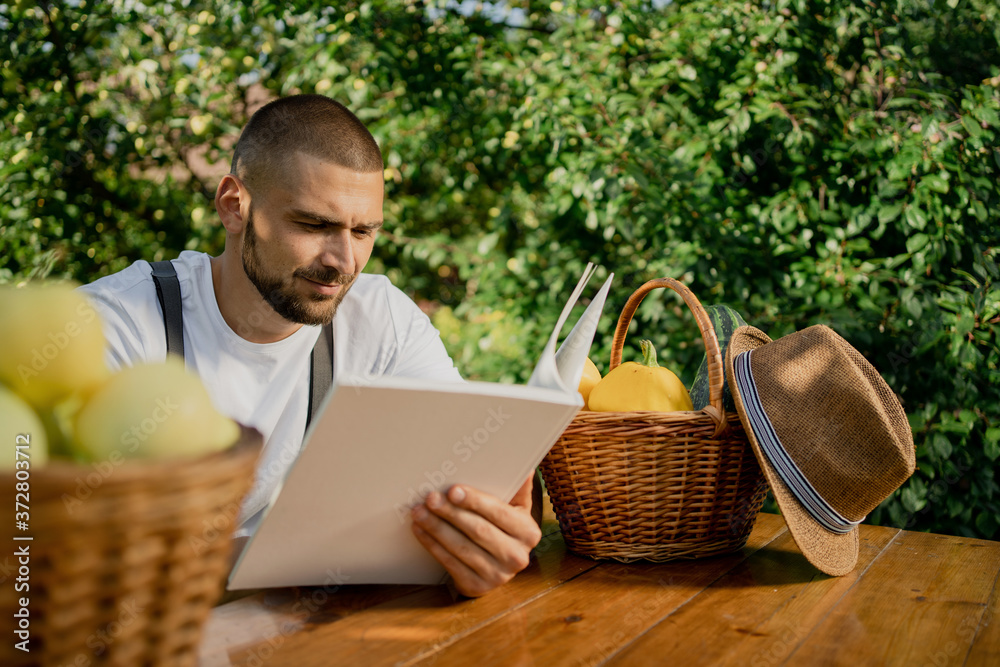 a young man with a basket in the garden sits at a table and reads a book on work a young man with a basket in the garden sits at a table and reads a book on work