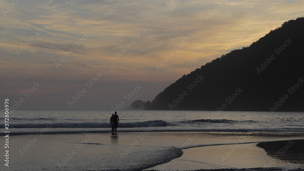 Couple standing in front the waves. Sunset beach, Praia do Sono, Paraty - Rio de Janeiro.