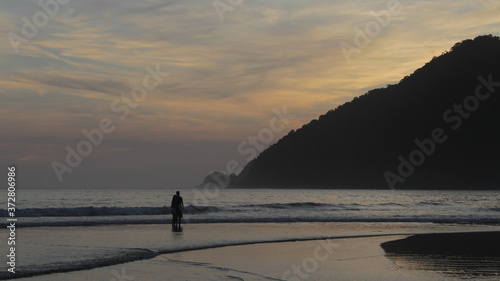 Couple standing in front the waves. Sunset beach, Praia do Sono, Paraty - Rio de Janeiro.
