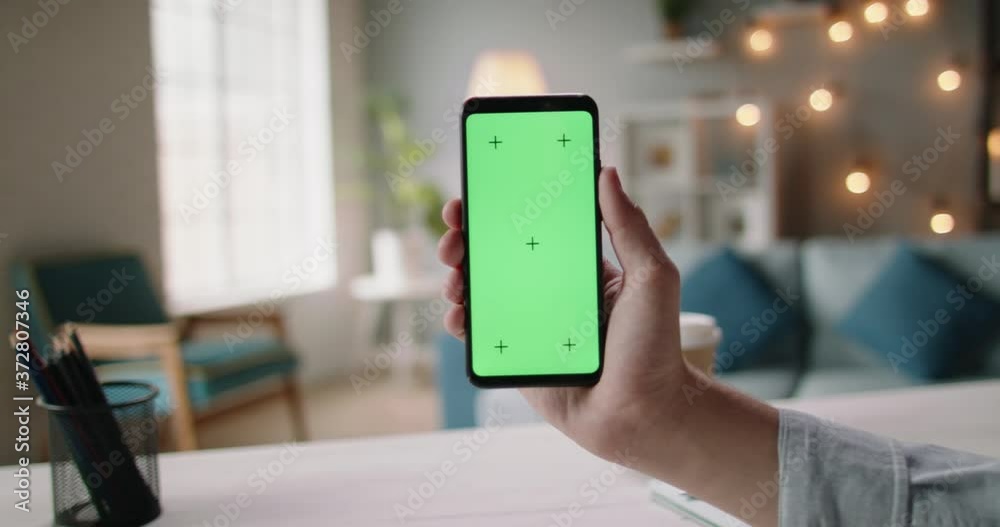 Close up shot of hand of guy holding a smartphone in cozy living room. A green screen mock up chroma key template 4k footage