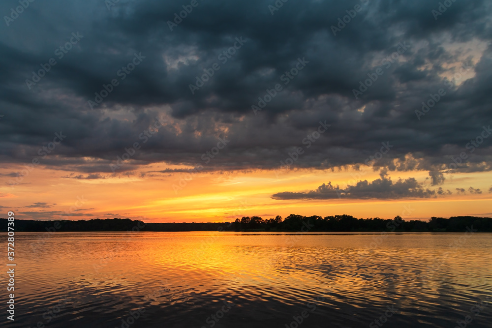 Sunset on the lake with vegetation in the background and sky full of clouds