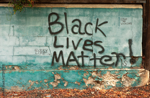 Painted graffiti sign on cement wall in gigantic letters reads "Black lives matter, stop the violence" and "every life."