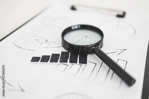 business analysis and statistics, desk with mixed graphs and charts on clipboard with magnifying glass on it