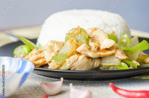 Chicken stir fried with green chilli and steamed rice in black dish. photo