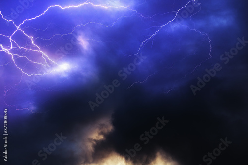 Purple stormy sky with thick dark clouds and bright lightning discharges. Aesthetic background for design with thunder clouds and lightning strikes.