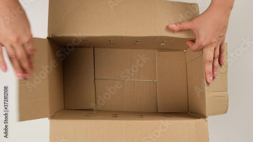 female hand opens brown cardboard box and fills with white filler for safe transportation, top view, moving concept