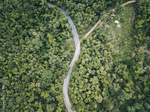 Aerial view of the road cut throug the green forest on the highland mountains in Chiang Rai province, Thailand. Beautiful view of the road from drone.