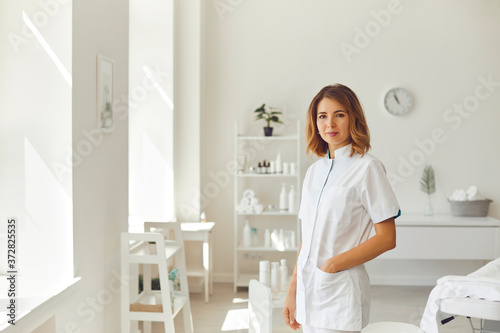 Smiling woman cosmetologist or dermatologist standing and looking at camera in beauty spa salon