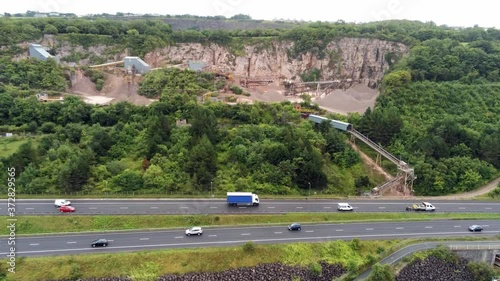 Aerial rising above North Wales expressway to CEMEX mining development site on lush greenery hillside photo