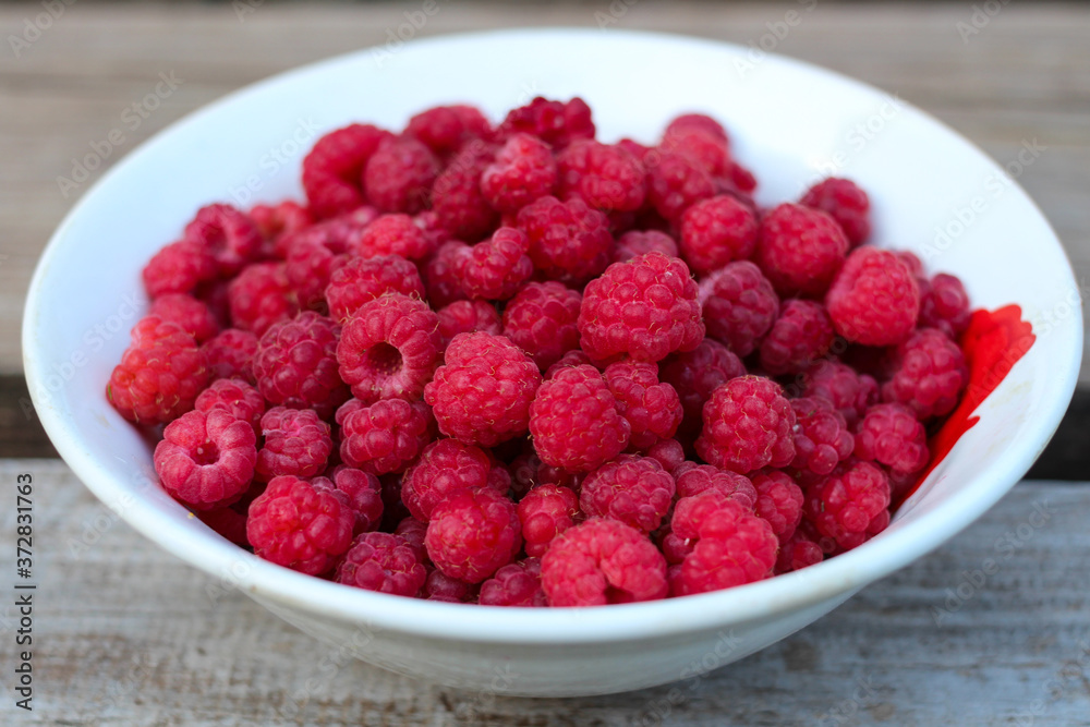 Close-up of a white plate with fresh forest raspberries, which stands on a gray wooden bench. Eco-friendly, healthy food. Close-up of a white plate with fresh forest raspberries, which stands on a gray wooden bench. Eco-friendly, healthy food.