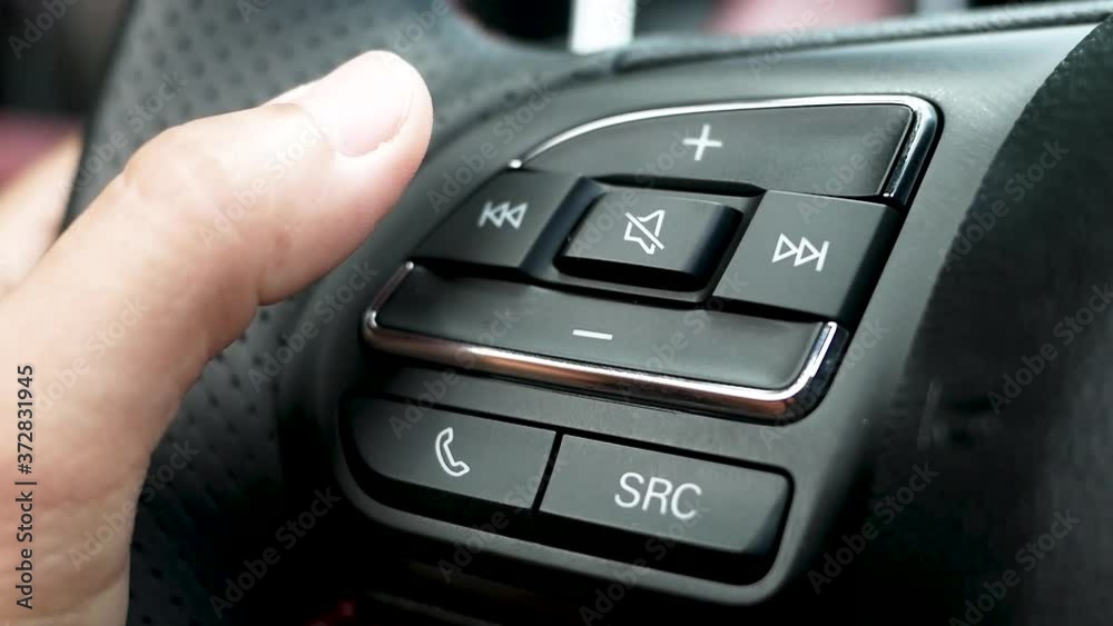 Close up of finger pressing the audio control buttons to increase or decrease the volume on the steering wheel when driving. Close up of finger pressing the audio control buttons to increase or decrease the volume on the steering wheel when driving.