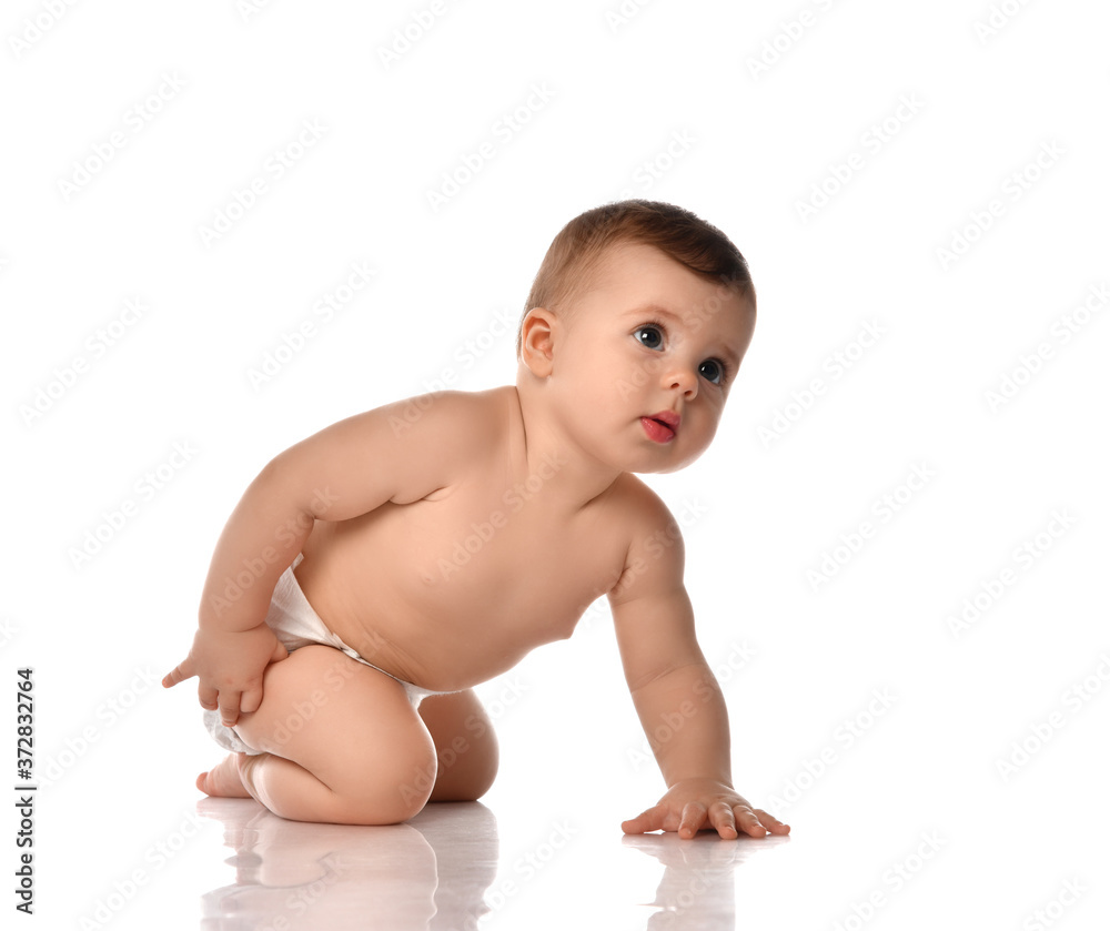 Attentive infant baby toddler naked in diaper stands on all fours touching his leg looking up trying to stand up Attentive infant baby toddler naked in diaper stands on all fours touching his leg looking up trying to stand up