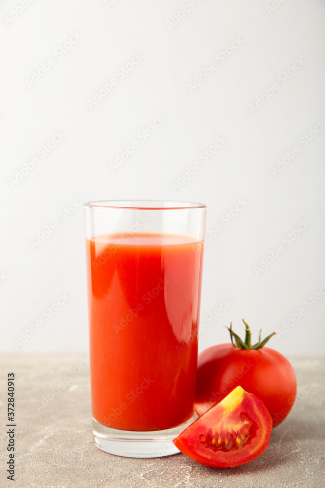 Tomato juice in the glass with tomatoes on grey Tomato juice in the glass with tomatoes on grey