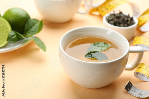 Cup of diet herbal tea with green leaves on orange background