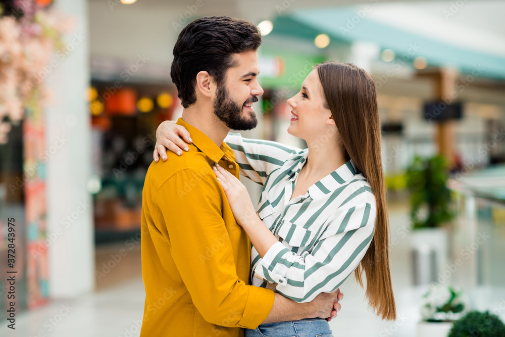 Profile side photo of positive gentle cute spouses girl husband hug cuddle enjoy valentine day rest relax wear yellow striped shirt in shopping mall center store Profile side photo of positive gentle cute spouses girl husband hug cuddle enjoy valentine day rest relax wear yellow striped shirt in shopping mall center store