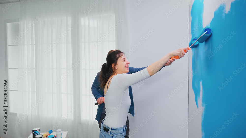 Happy family painting apartment wall with blue paint using roller brush. Home decoration and renovation in cozy apartment flat, repair and makeover Happy family painting apartment wall with blue paint using roller brush. Home decoration and renovation in cozy apartment flat, repair and makeover