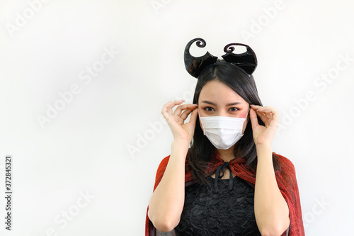 Portrait of beautiful young asian woman wearing red dress and black shawl and protection face mask against coronavirus on gray colour background - Halloween party concept