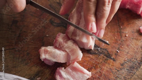 Lady slicing streaky pork on wooden board with small knife. Traditional way. unhealthy and full of fat. homemade preparation with a lot of fatty. Raw meat.