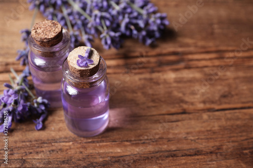 Bottles of essential oil and lavender flowers on wooden table. Space for text