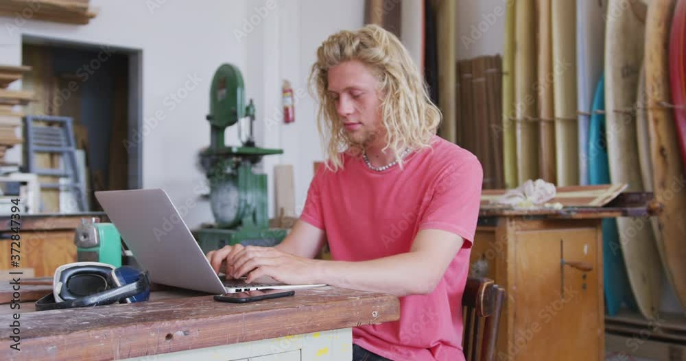 Caucasian male surfboard maker working on his laptop Caucasian male surfboard maker working on his laptop