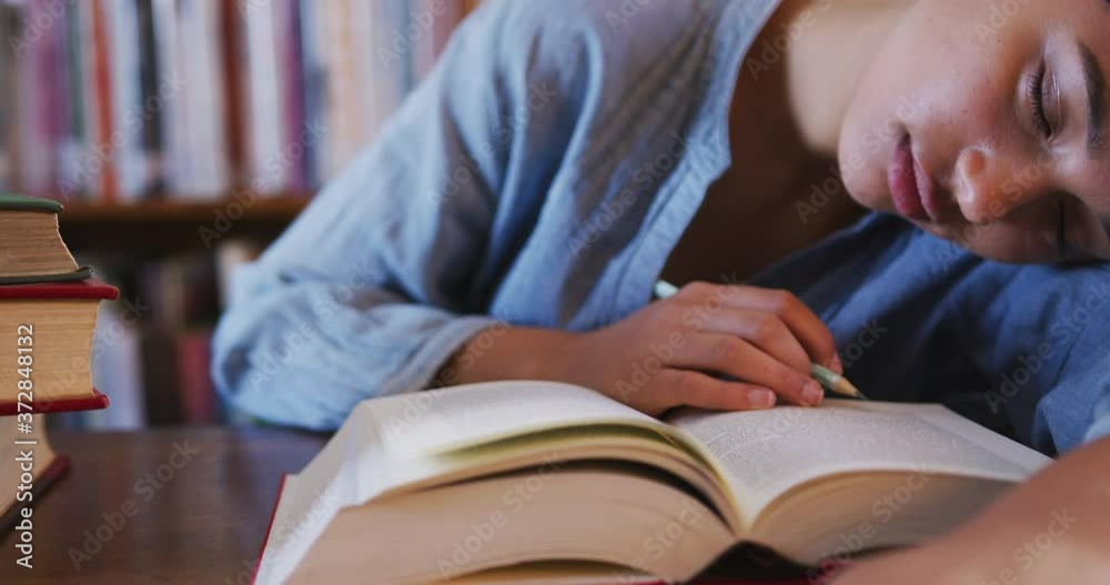 Asian female student wearing a blue hijab sitting at a desk with an open book and sleeping Asian female student wearing a blue hijab sitting at a desk with an open book and sleeping