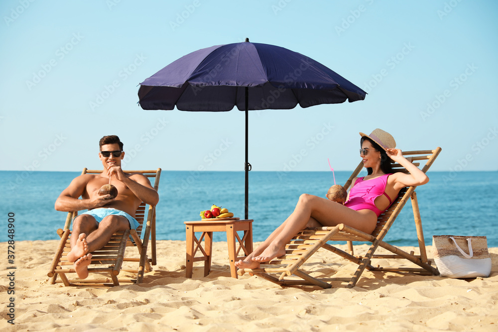 Couple with drinks resting on sunny beach at resort Couple with drinks resting on sunny beach at resort