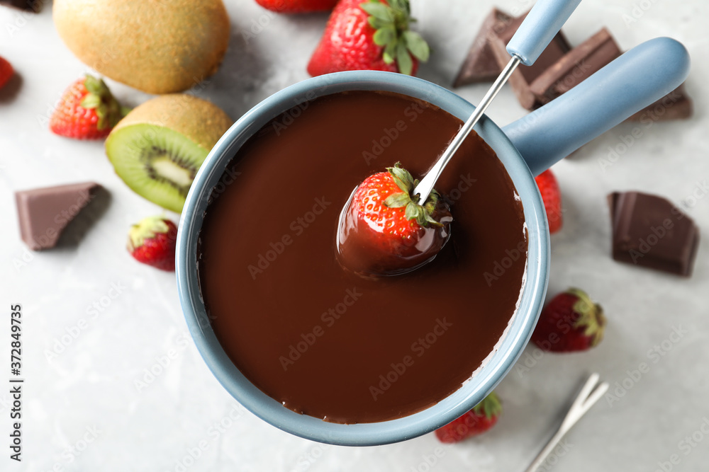 Dipping strawberry into fondue pot with chocolate on light table, top view Dipping strawberry into fondue pot with chocolate on light table, top view