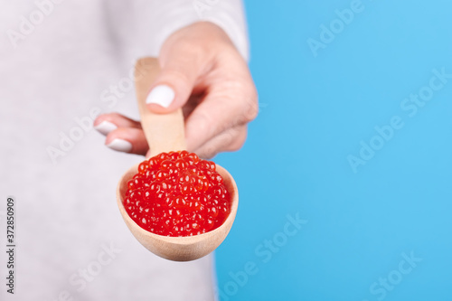 Salmon fish caviar, seafood on wooden spoon in hand, isolated on blue background.