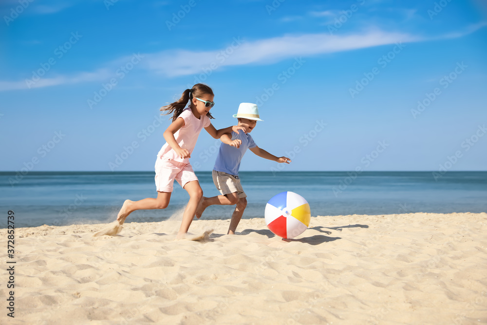 Cute little children playing with inflatable ball on sandy beach
