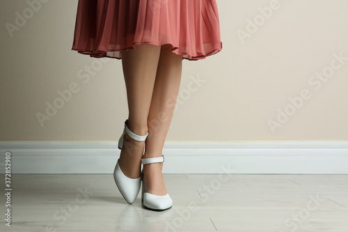 Woman wearing stylish shoes near beige wall indoors, closeup