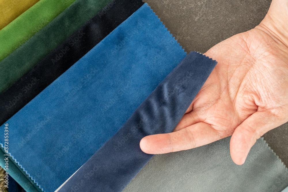 White male hand with palm up holding a blue velvet fabric sample seen top down