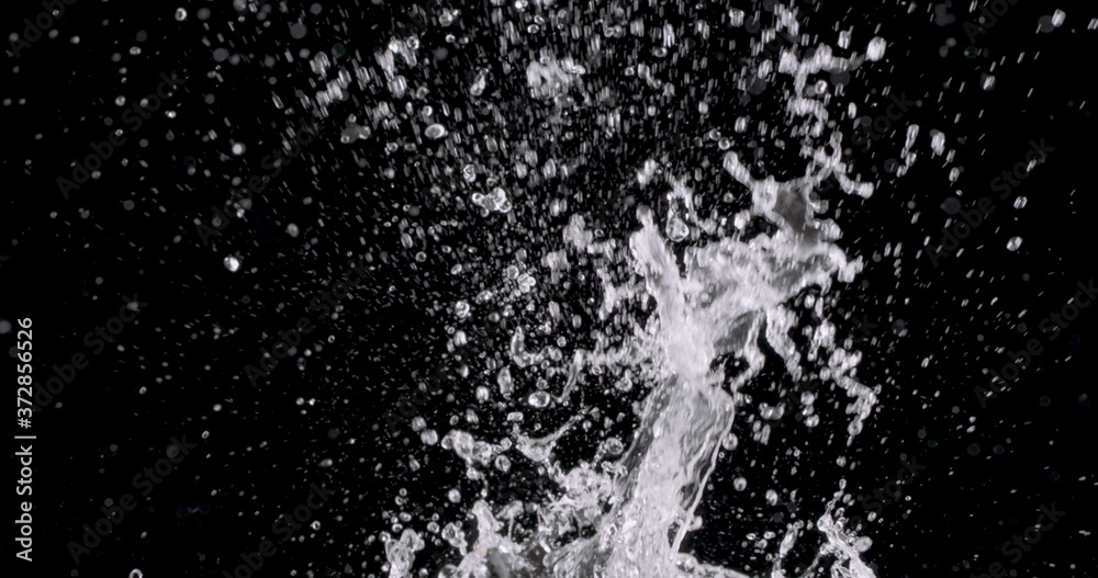 spray of water bursting from the bottom of the screen and water droplets fall down against the black background.