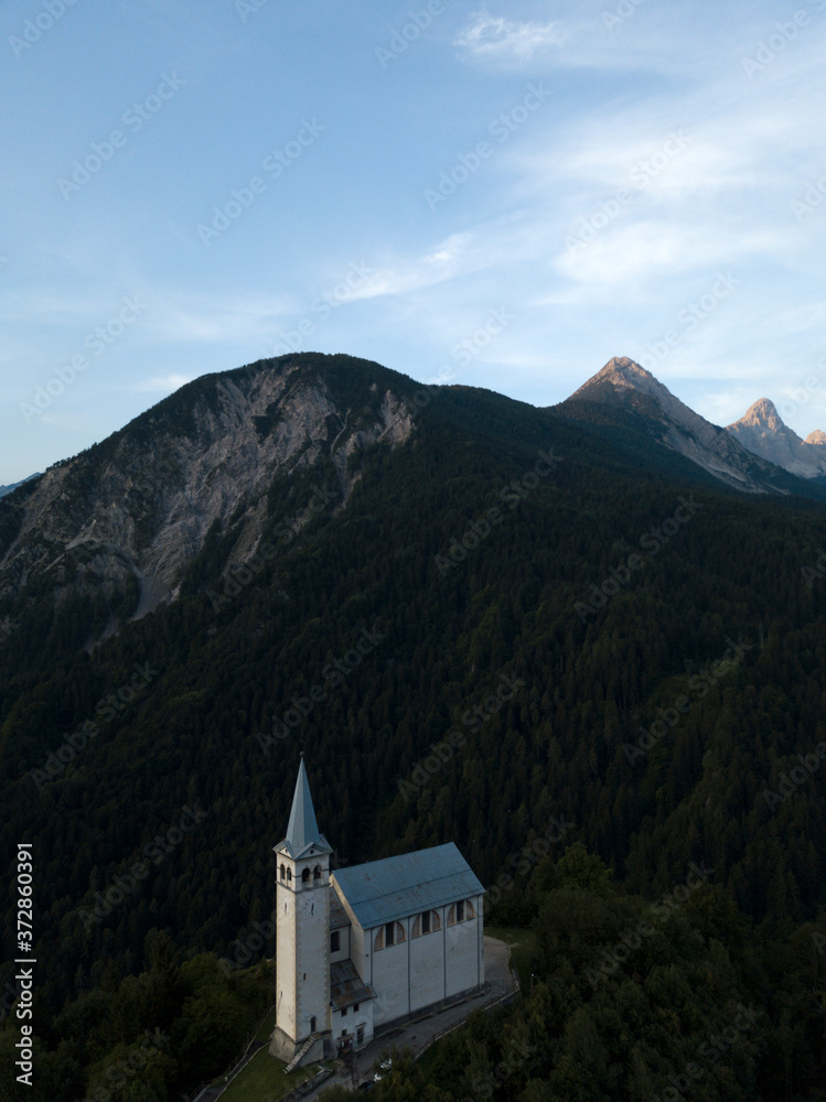 Aerial view of tyrolean church in Alps mountains Dolomites Italy, South Tyrol, Europe. Early morning sunrise, blue sky, high mountain range, clouds. Summer.