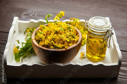 Glass jar with hypericum or St Johns wort oil extract and bowl with fresh flowers
