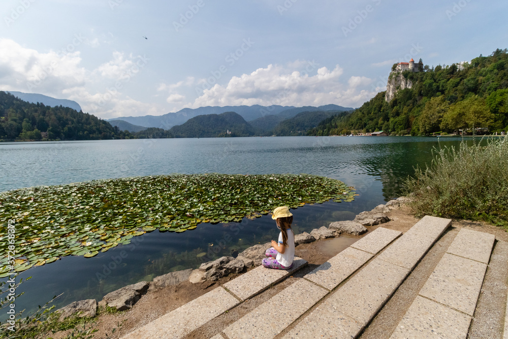 Fototapeta premium A small girl is sitting on the bank of lake bled in slovenia