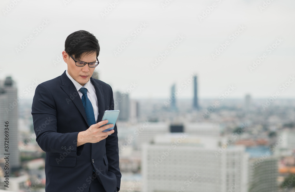 Young asian businessman using smartphone to connecting or reading text with his work on urban city background. Young asian businessman using smartphone to connecting or reading text with his work on urban city background.