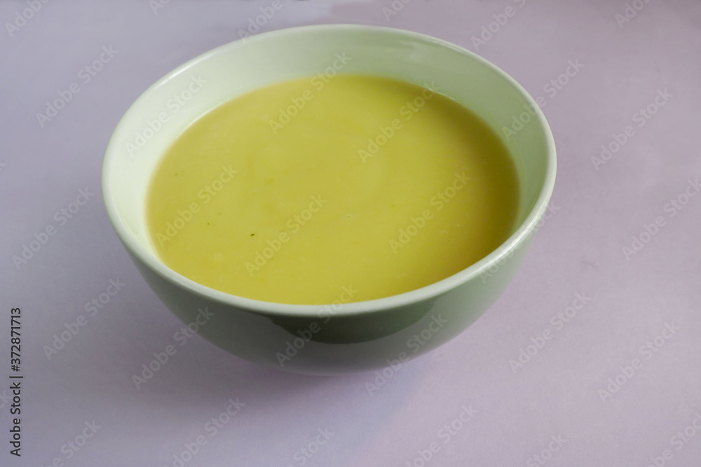 green plate with cream soup of zucchini, potatoes, cream, onions on a purple background of side view . cooking gluten-free food at home green plate with cream soup of zucchini, potatoes, cream, onions on a purple background of side view . cooking gluten-free food at home