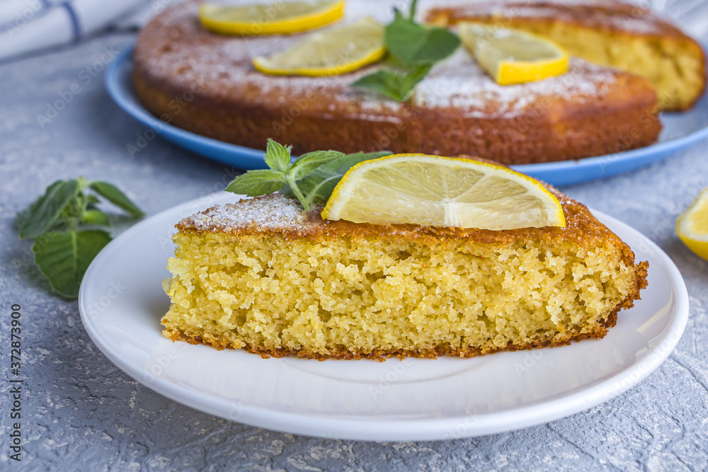 Cutting up and piece of freshly baked lemon pie, tart or semolina cake on plate served lemon wedges and mint. Homemade baking. Close up, copy space for text Cutting up and piece of freshly baked lemon pie, tart or semolina cake on plate served lemon wedges and mint. Homemade baking. Close up, copy space for text