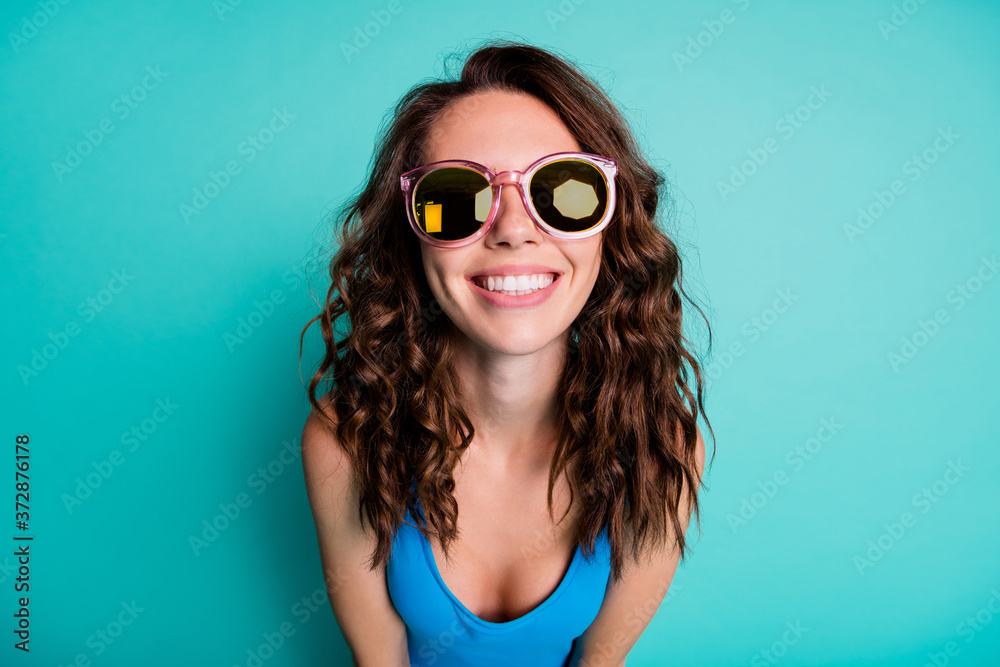Closeup photo of shiny lovely girlish lady model beaming smile round pink sun specs curly hairstyle bright playful carefree beach resort wear blue swimsuit isolated turquoise color background