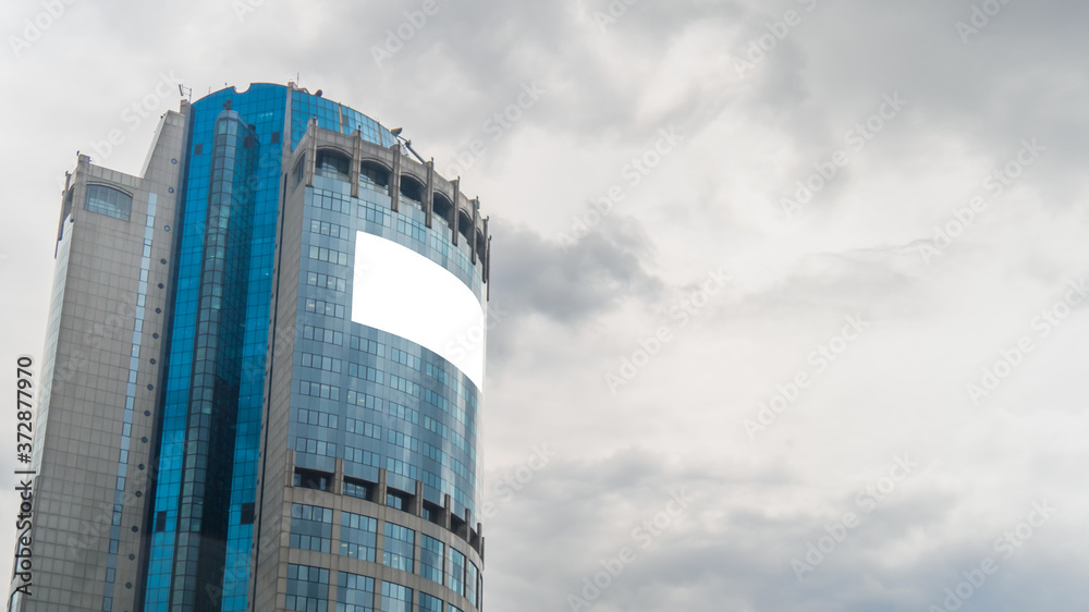 Obraz premium Daylight, overcast. Consumerism, mockup, background, isolated white screen, copyspace concept. Mock up image - blank white billboard or large advertising display on tall building, glass skyscraper