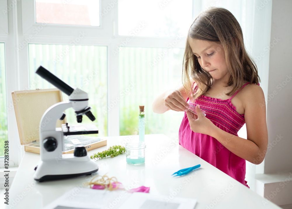 Pretty blonde little girl working with test tube and microscope. The kid learning science in the school laboratory or at home. Child looking make experiment with microscope on the table. Pretty blonde little girl working with test tube and microscope. The kid learning science in the school laboratory or at home. Child looking make experiment with microscope on the table.