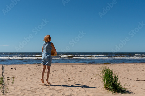 Jumping happy woman by the sea with a beach hat in her hands