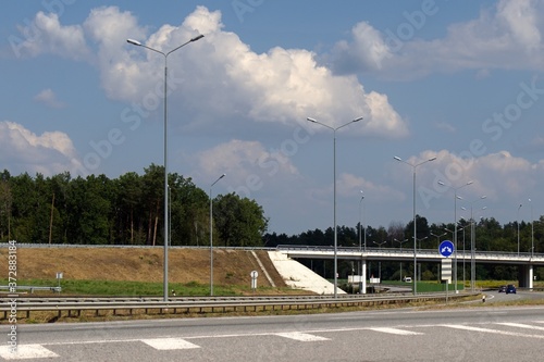 overpass over the freeway, lighting pillars along the road, blurred foreground, blue sky with white clouds