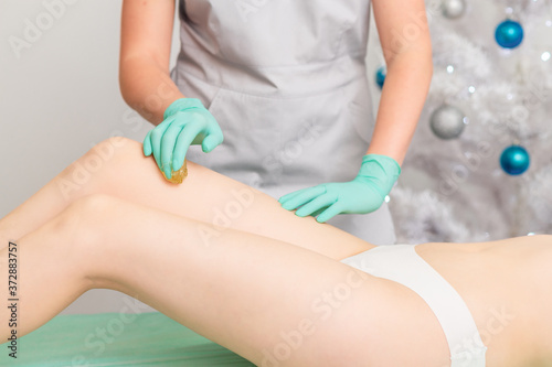 Beautician waxing female legs in spa center.