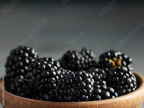 Juicy ripe blackberries on a wooden plate on a gray background. Dark foodphoto. Copy space. Healthy food concept