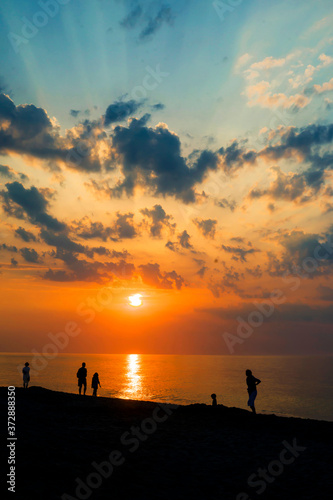 Contours of people walking by the sea at sunset against the backdrop of dramatic clouds