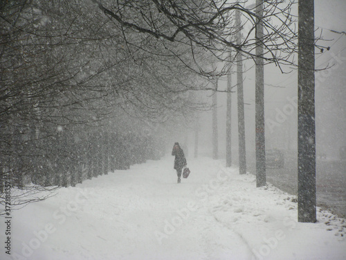Kobieta idąca w wichurze po zaśnieżonym chodniku