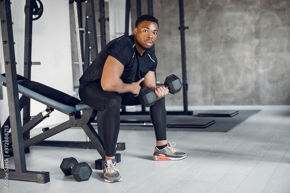 Sports man in the gym. A black man performs exercises. Guy in a black t-shirt Sports man in the gym. A black man performs exercises. Guy in a black t-shirt